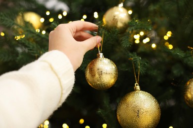 Woman decorating fir tree with golden Christmas ball, closeup