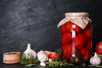 Photo of Glass jar of pickled tomatoes and ingredients on black table. Space for text