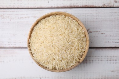Raw rice in bowl on light wooden table, top view