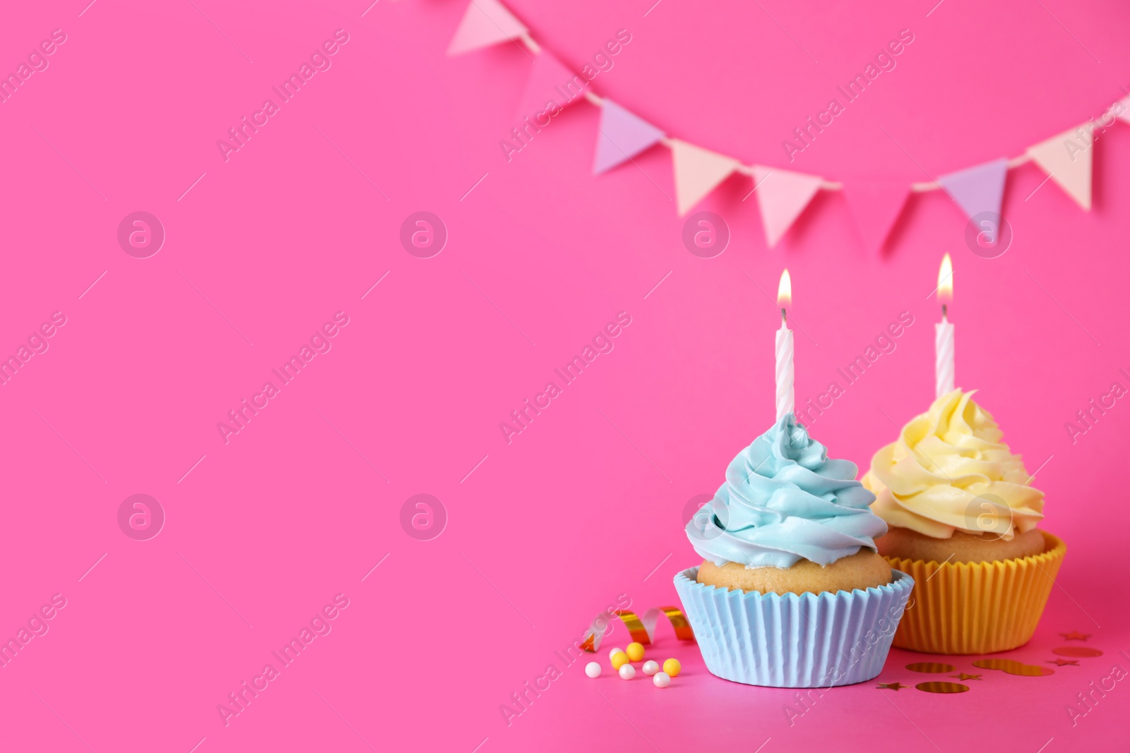 Photo of Delicious birthday cupcakes with burning candles, sprinkles and confetti on pink background, space for text