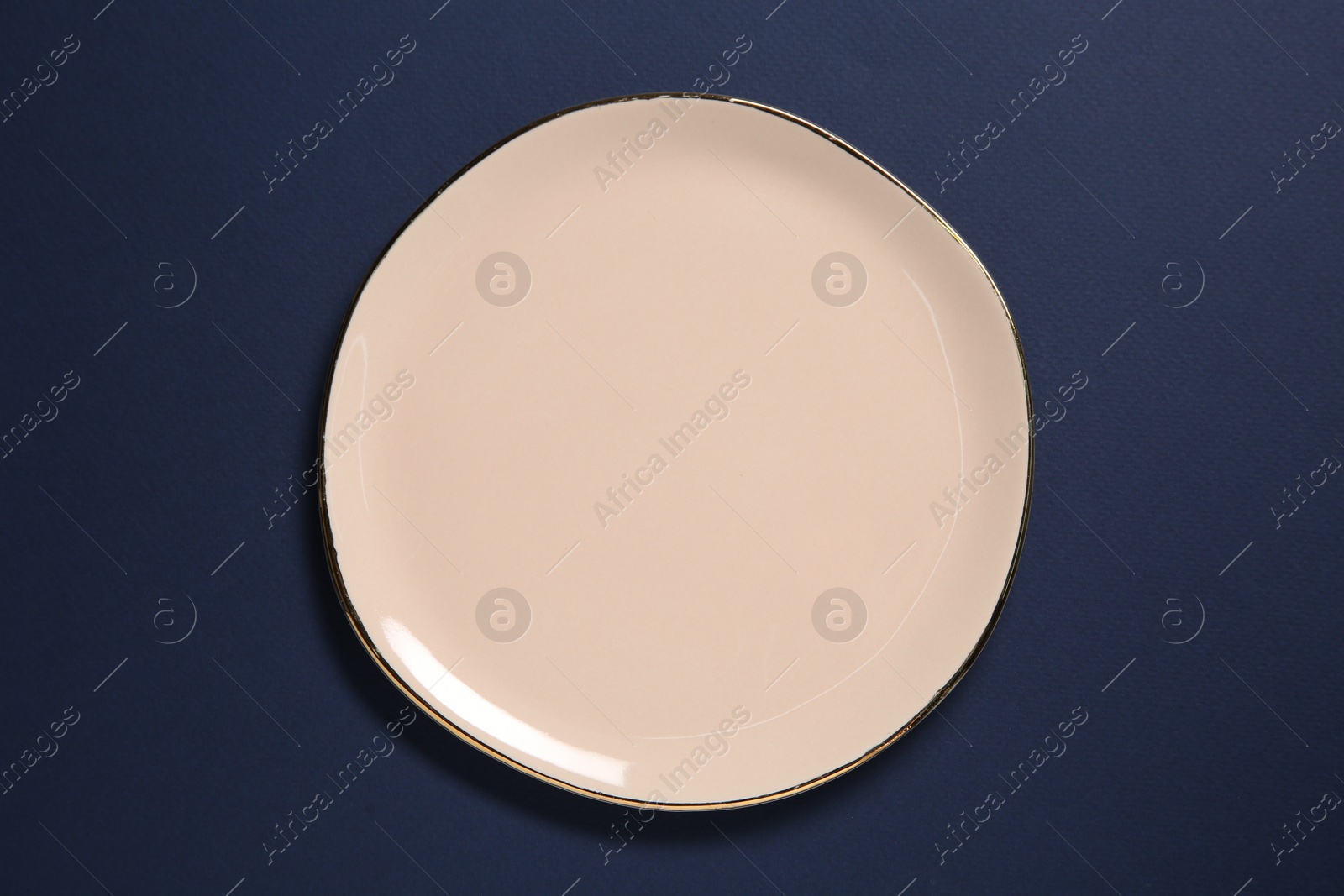 Photo of One beige ceramic plate on dark blue background, top view