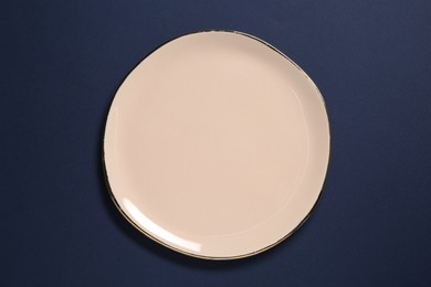 Photo of One beige ceramic plate on dark blue background, top view