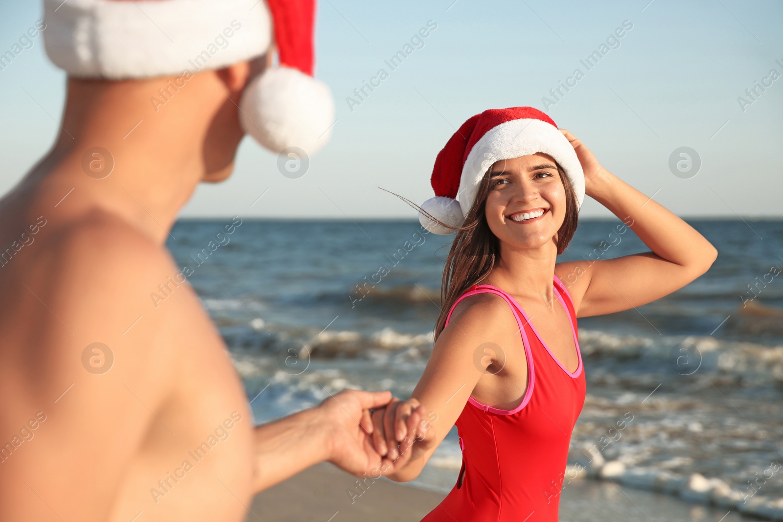 Photo of Happy couple with Santa hats together on beach. Christmas vacation