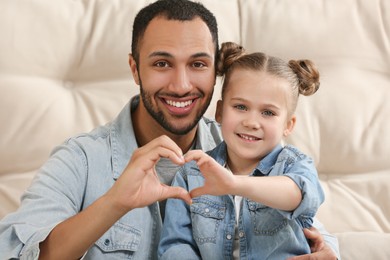 Photo of Little girl and her father making heart with hands. International family