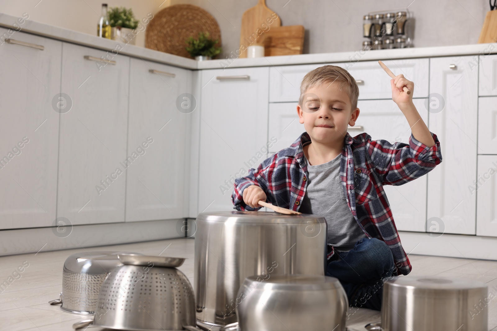 Photo of Little boy pretending to play drums on pots in kitchen