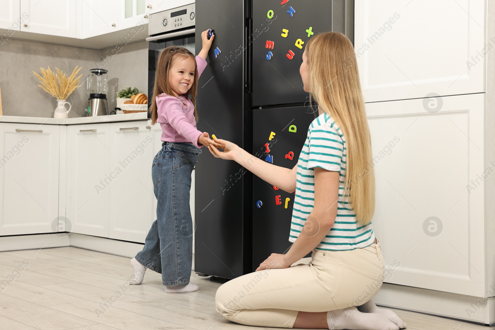 Photo of Mom and daughter putting magnetic letters on fridge at home. Learning alphabet