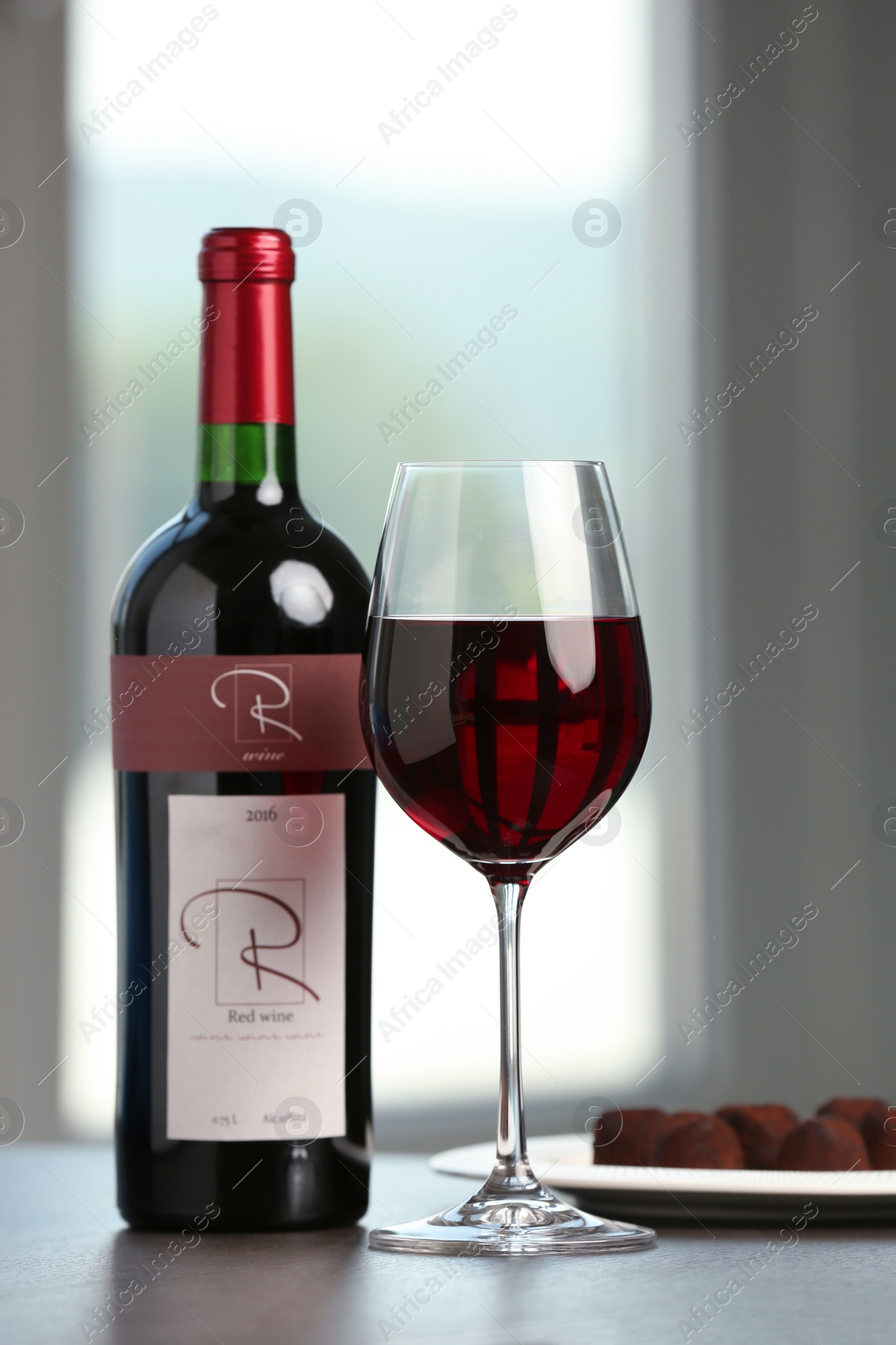 Photo of Bottle and glass of red wine with chocolate candies on wooden table indoors