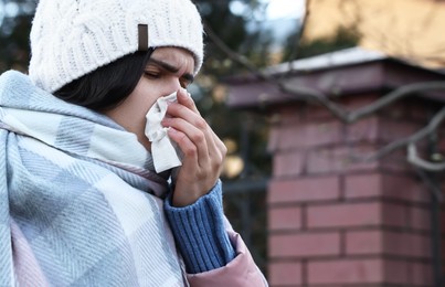 Photo of Woman with tissue blowing runny nose outdoors, space for text. Cold symptom