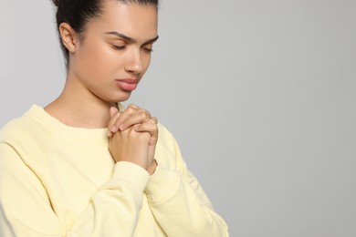 Photo of African American woman with clasped hands praying to God on light grey background. Space for text