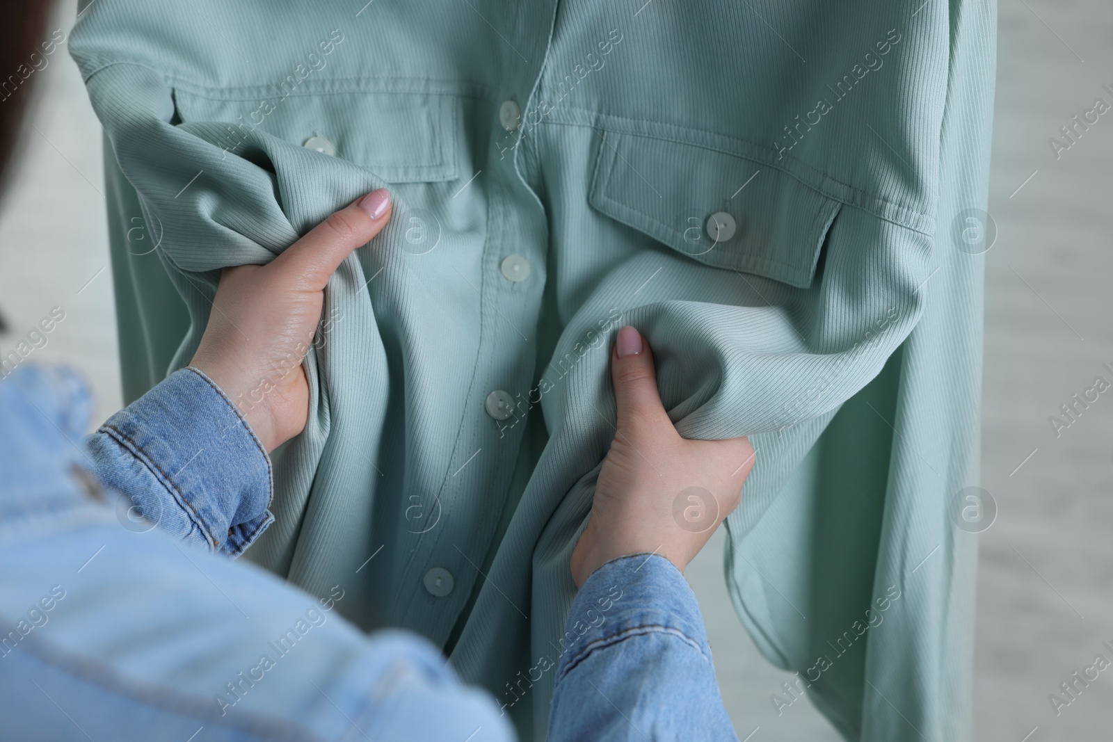 Photo of Woman touching shirt made of soft turquoise fabric indoors, closeup