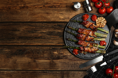 Photo of Oven baked asparagus wrapped with bacon on wooden table, flat lay. Space for text