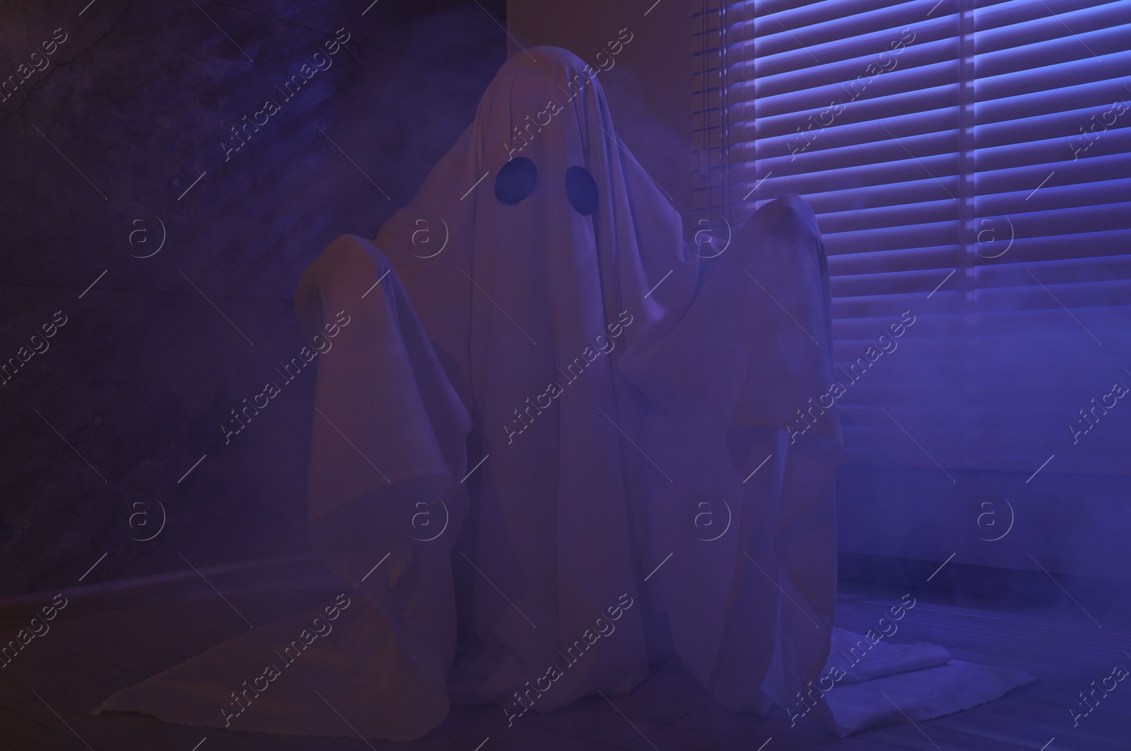 Photo of Creepy ghost. Woman covered with sheet near window in color lights