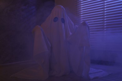 Creepy ghost. Woman covered with sheet near window in color lights