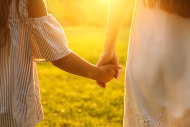 Photo of Little girl and her mother holding hands in park, closeup. Happy family