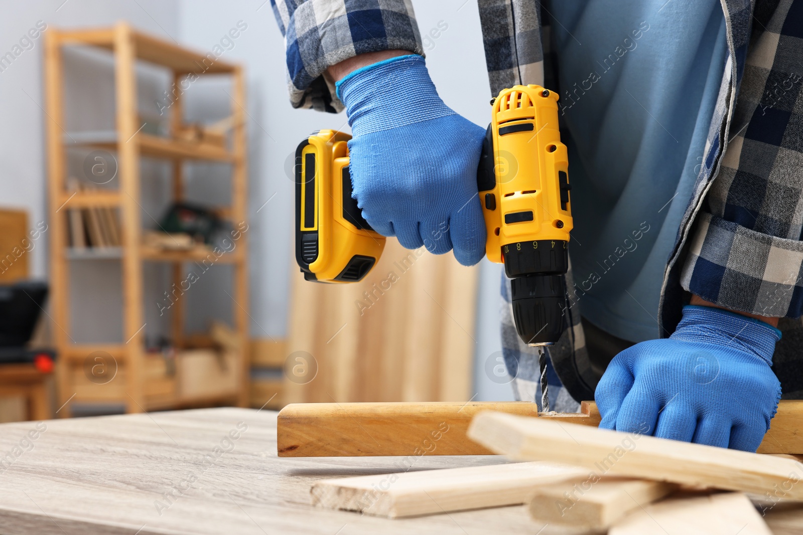 Photo of Young handyman working with electric drill at table in workshop, closeup