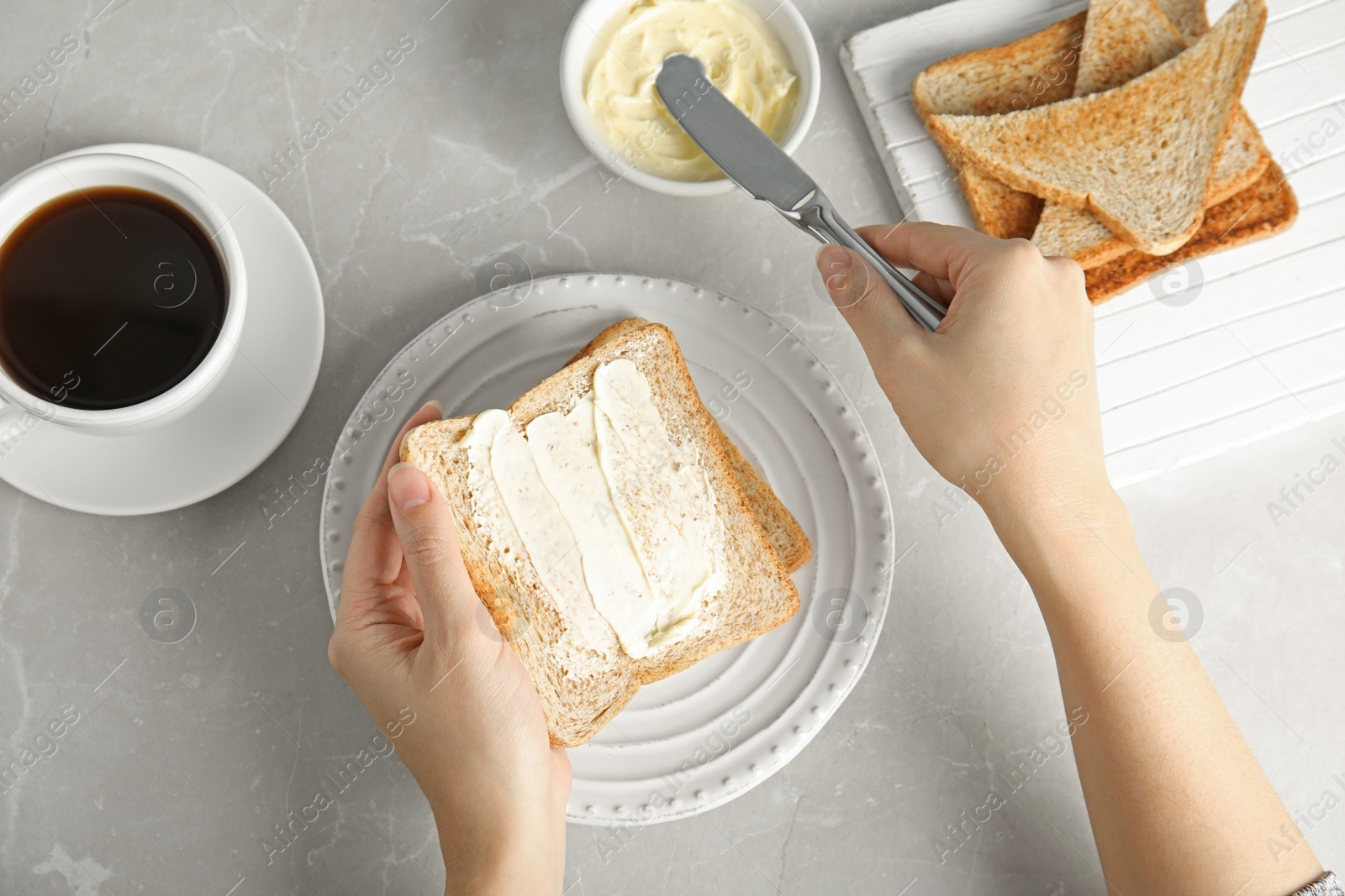 Photo of Woman spreading butter onto slice of bread over grey table, top view