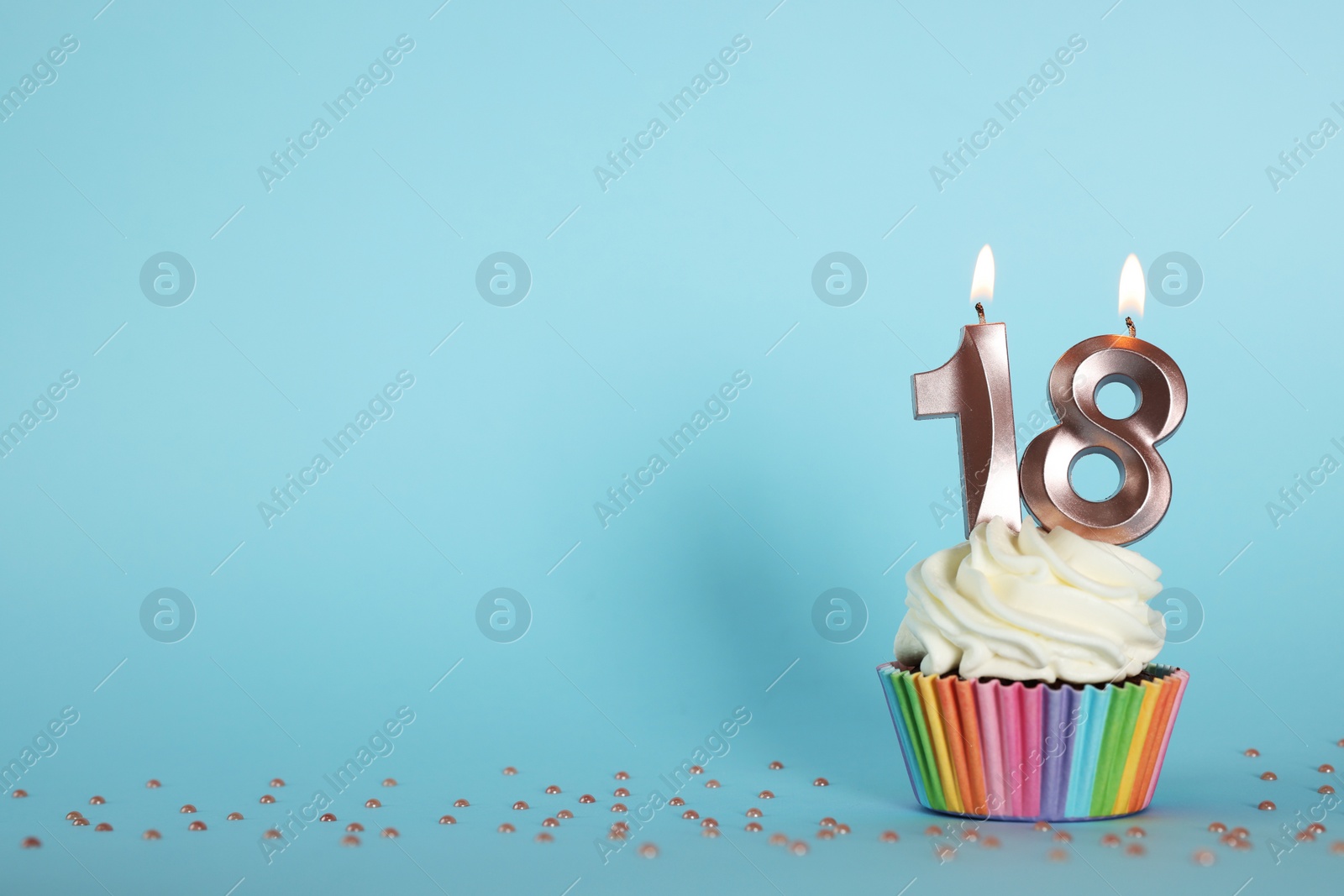 Photo of Delicious cupcake with number shaped candles on light blue background, space for text. Coming of age party - 18th birthday