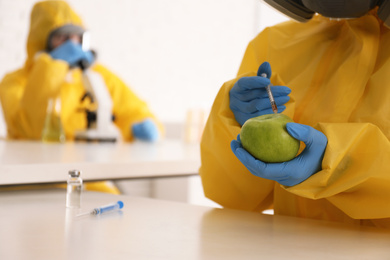 Scientist in chemical protective suit injecting apple at laboratory, closeup with space for text