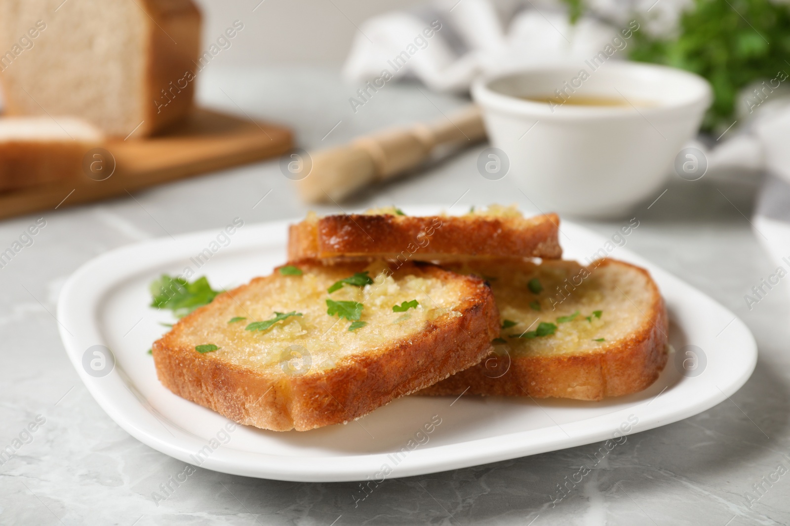 Photo of Slices of toasted bread with garlic and herb on light grey marble table, closeup