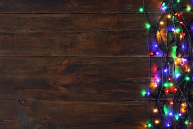 Photo of Glowing Christmas lights on brown wooden background, top view. Space for text