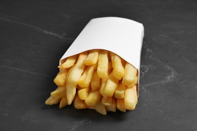 Delicious french fries in paper box on black table, closeup