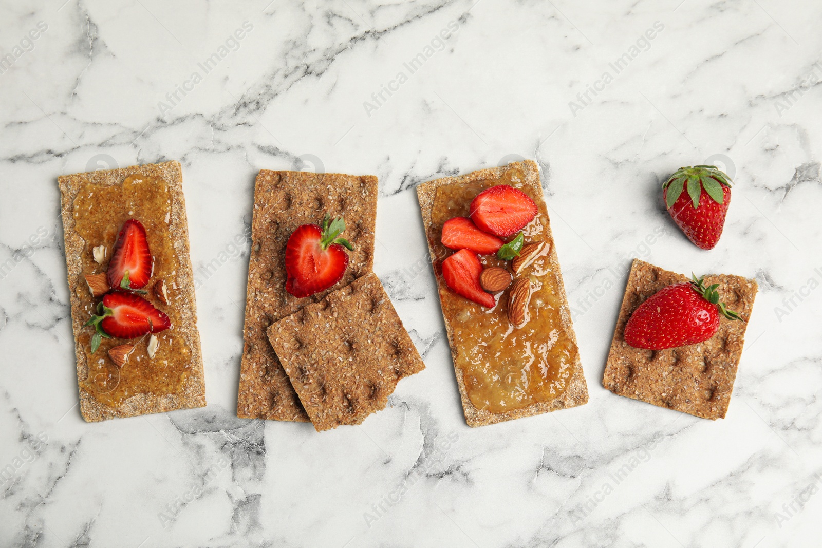 Photo of Fresh rye crispbreads with jam, strawberries and almonds on white marble table, flat lay