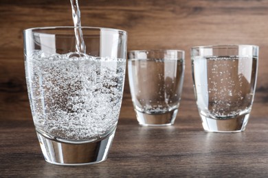 Photo of Pouring soda water into glass on wooden table