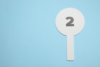 Photo of Auction paddle with number 2 on light blue background, top view. Space for text