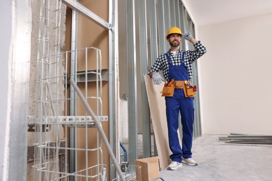 Photo of Professional builder in uniform with tool belt indoors