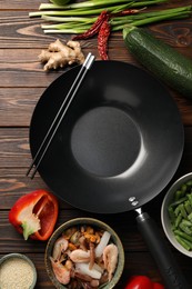 Black wok, chopsticks and products on wooden table, flat lay