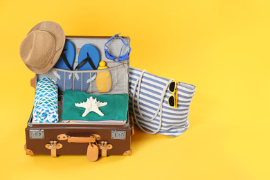 Photo of Bag and open vintage suitcase with different beach objects packed for summer vacation on orange background