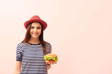 Photo of Young woman with tasty burger on color background. Space for text