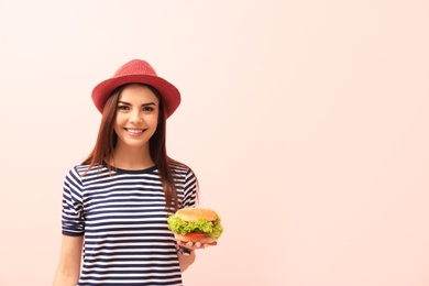 Young woman with tasty burger on color background. Space for text