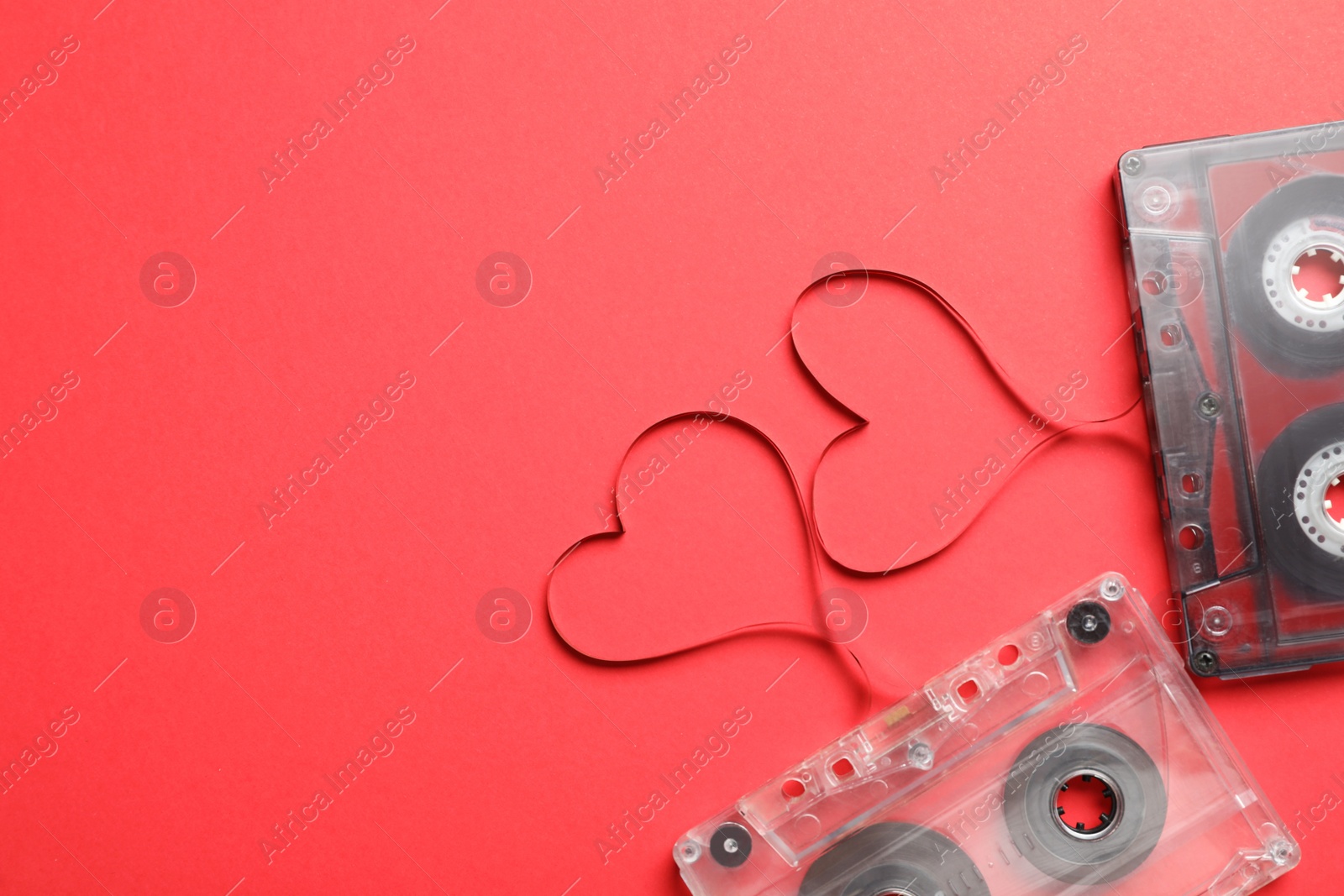 Photo of Music cassettes and hearts made of tape on red background, flat lay with space for text. Listening love songs