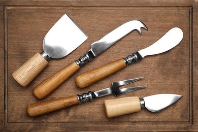 Cheese knives and fork on wooden board, flat lay