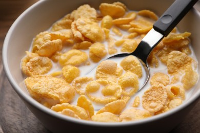 Photo of Spoon with tasty cornflakes and milk in bowl on table, closeup