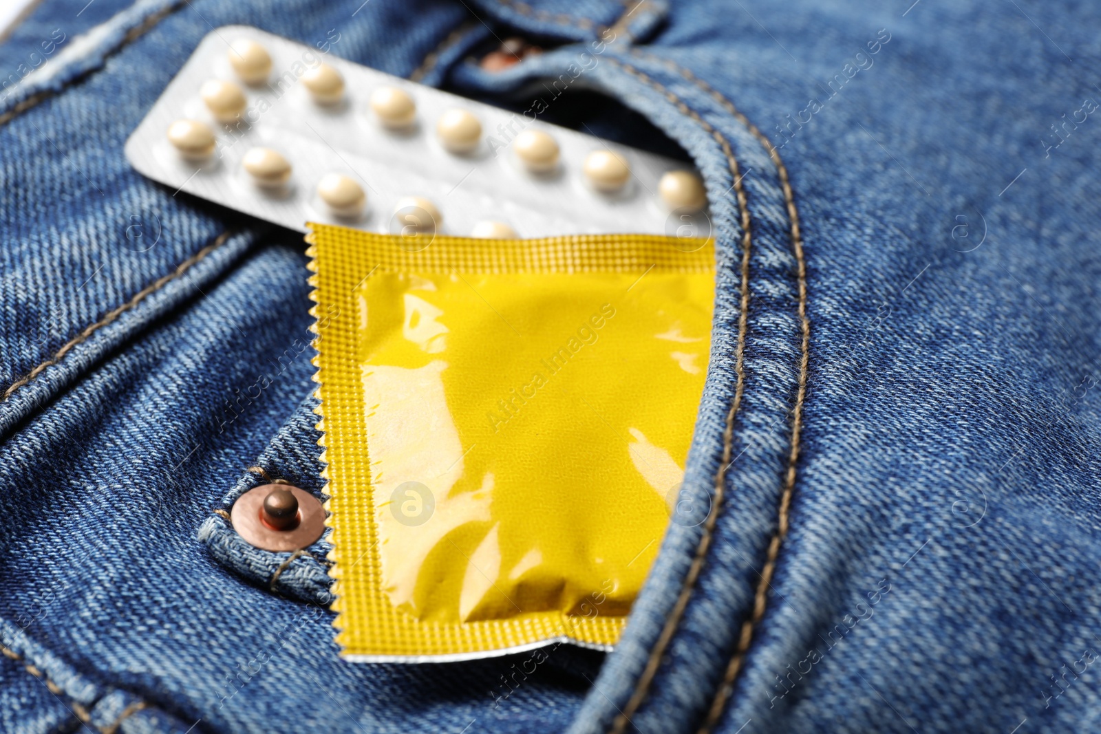 Photo of Yellow condom and birth control pills in pocket of jeans, closeup. Safe sex concept