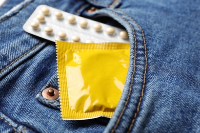 Photo of Yellow condom and birth control pills in pocket of jeans, closeup. Safe sex concept