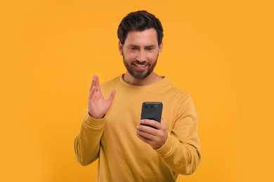 Photo of Handsome bearded using smartphone on orange background