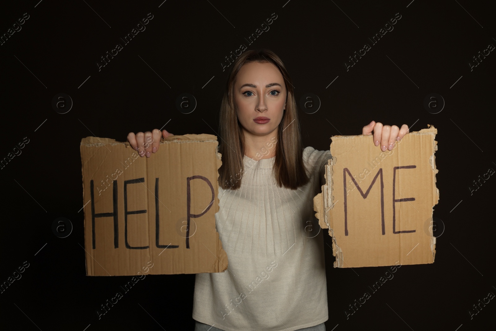 Photo of Unhappy young woman with HELP ME sign on dark background