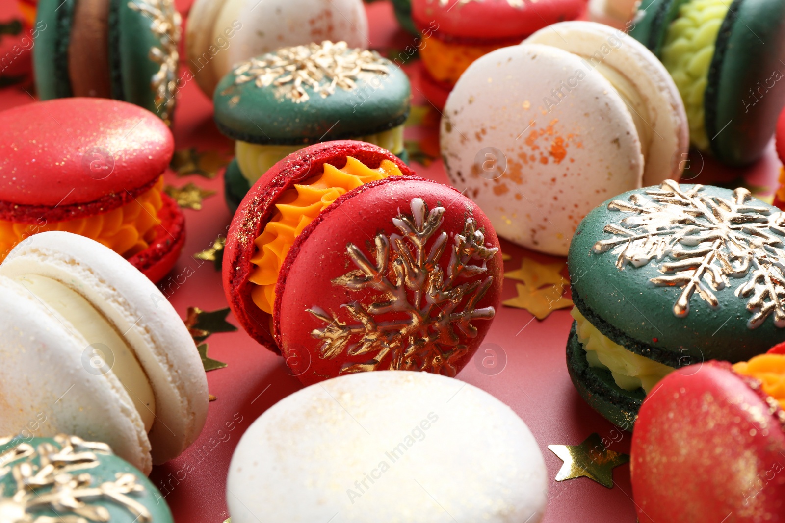 Photo of Beautifully decorated Christmas macarons and confetti on red background, closeup