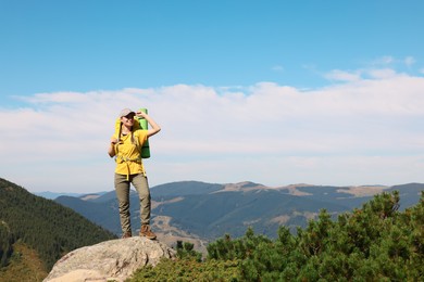 Photo of Young woman with backpack on rocky peak in mountains