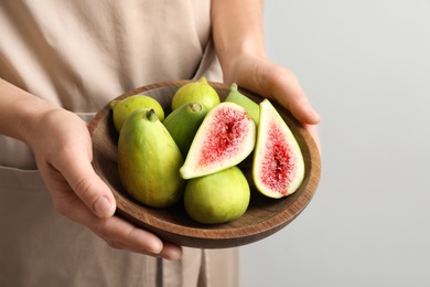 Photo of Woman holding bowl with fresh ripe figs on light background