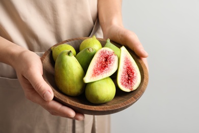 Woman holding bowl with fresh ripe figs on light background