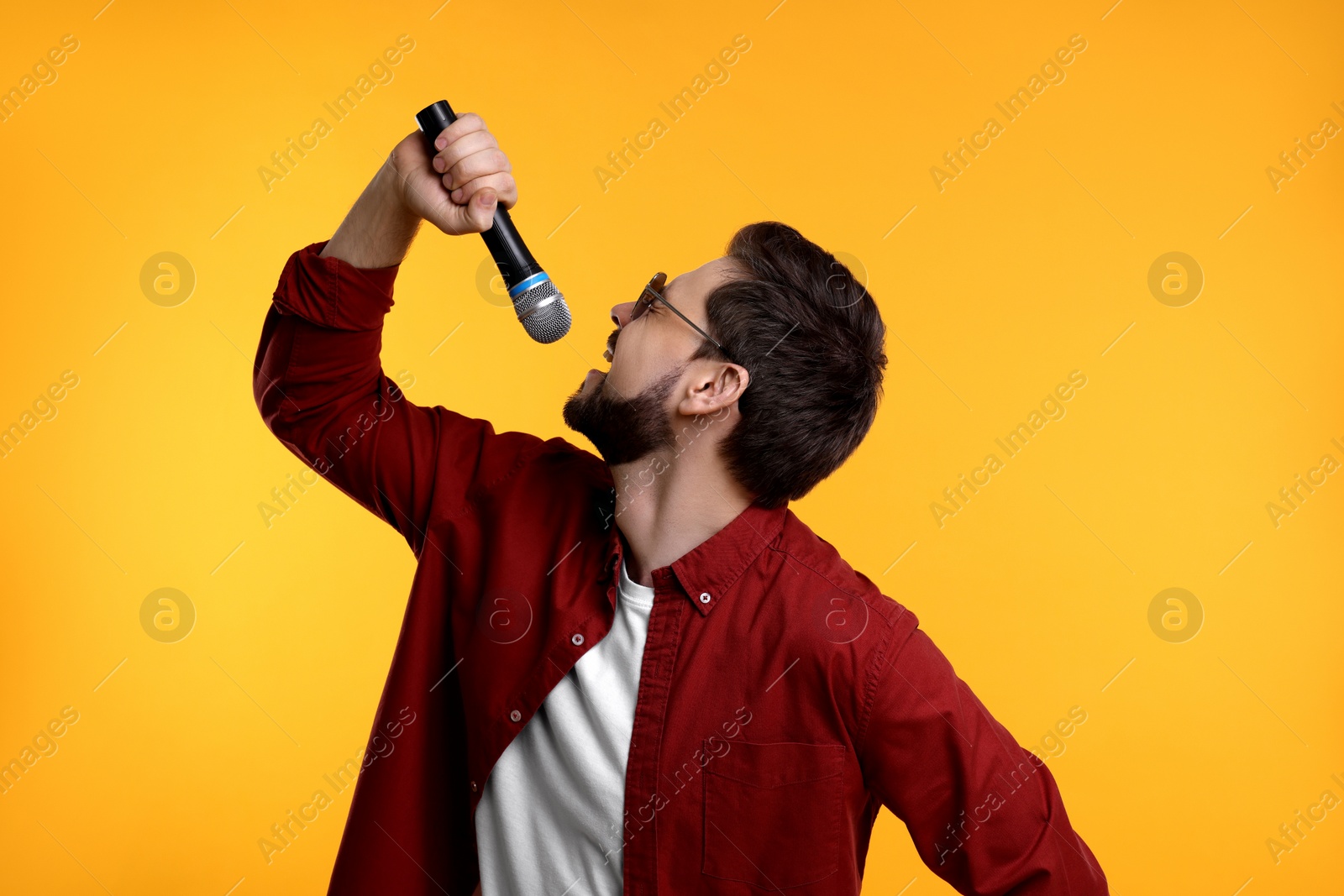 Photo of Handsome man with sunglasses and microphone singing on yellow background