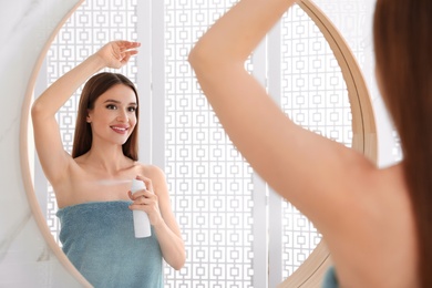 Photo of Beautiful young woman applying deodorant after shower in bathroom