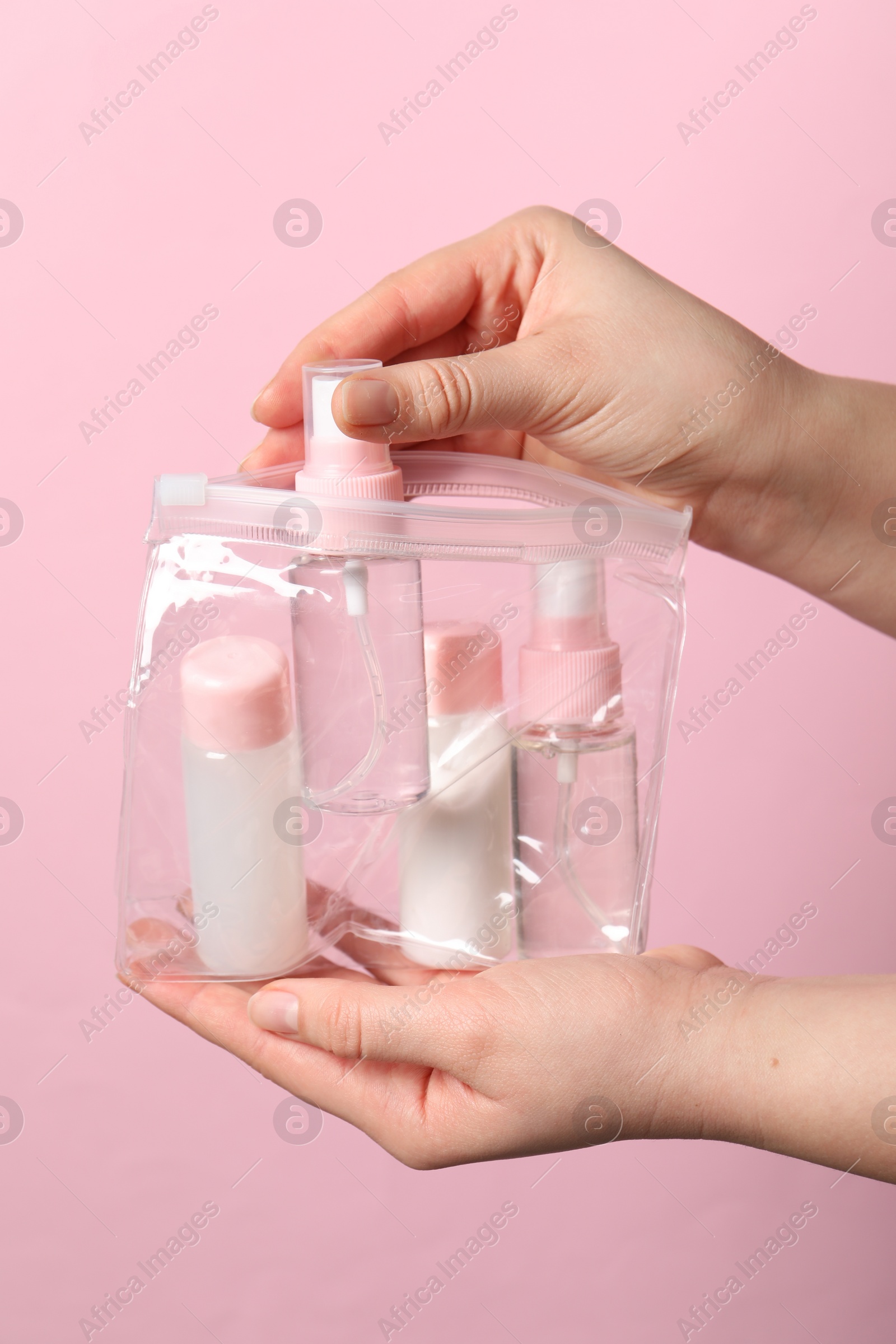 Photo of Cosmetic travel kit. Woman putting small bottle with personal care product into plastic bag against pink background, closeup