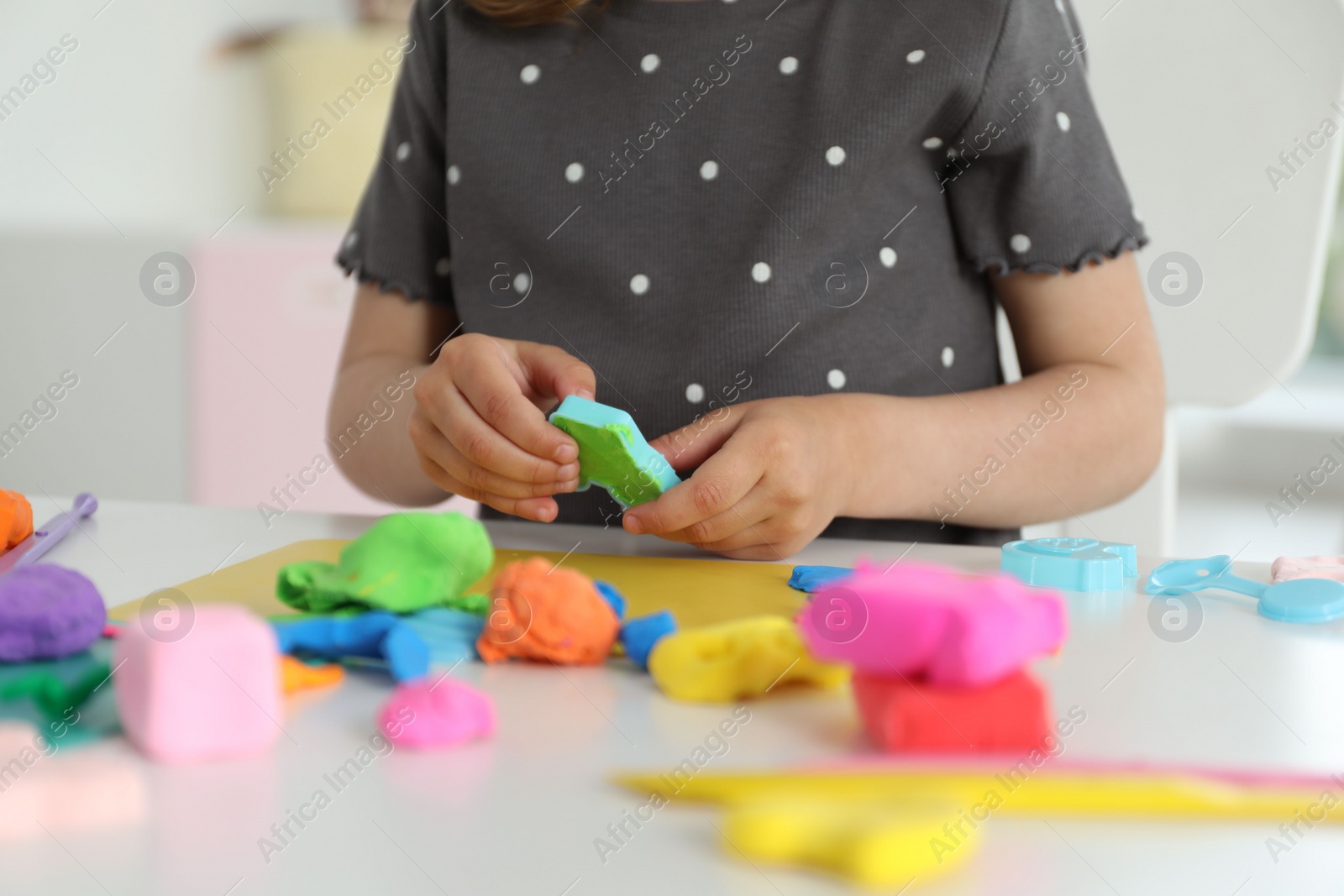 Photo of Little girl sculpting with play dough at table indoors, closeup