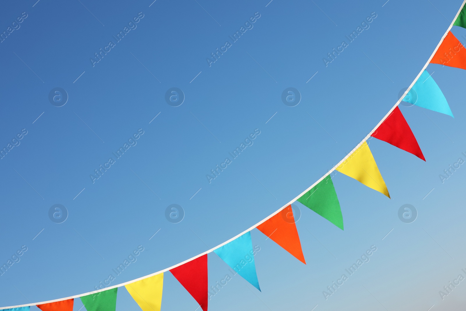 Photo of Bunting with colorful triangular flags against blue sky. Space for text