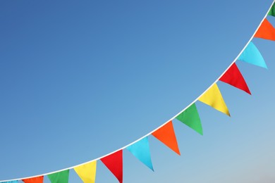 Bunting with colorful triangular flags against blue sky. Space for text